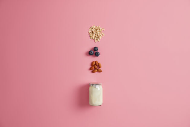 品种多种健康的早餐原料酸奶 麦片粥 蓝莓 杏仁坚果混合在粉红色的背景上美味的产品 准备美味的营养粥吃的概念松香燕麦膳食