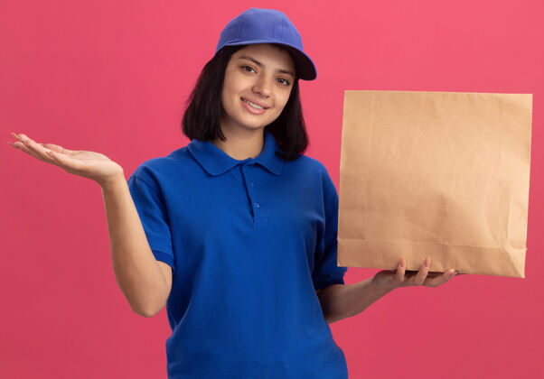 自信身穿蓝色制服 头戴礼帽的年轻送货员微笑着自信地站在粉红色的墙上制服展示年轻