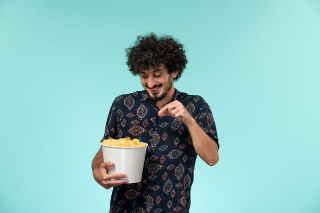 肖像前视图年轻人拿着土豆cips在蓝墙上电影院男电影餐具咖啡