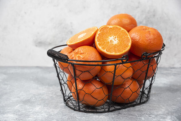 天然石桌上放着一个装满多汁橙子的金属黑色篮子甜点柑橘成熟