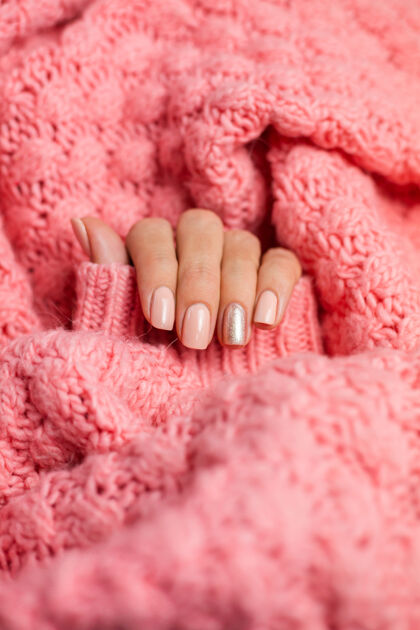 健康漂亮的裸色美甲 一个手指闪亮的金色 在针织粉色羊毛枕头的背景下顶部美甲手指