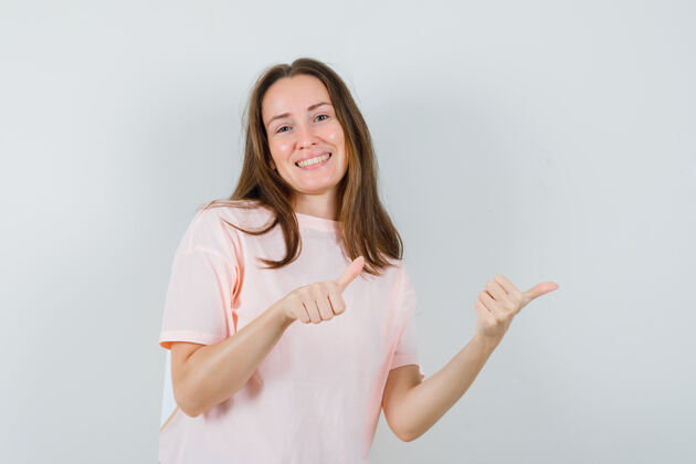 女士穿着粉色t恤的年轻女士指着侧面竖起大拇指 看起来很活泼活泼壁板指向