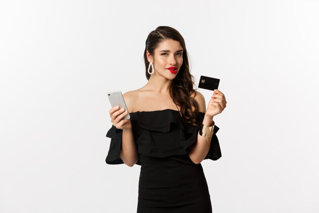 莫比尔时尚购物理念红唇女人 黑衣女人 想着买什么 手里拿着信用卡和手机 站在白色的背景上表情信用卡口红