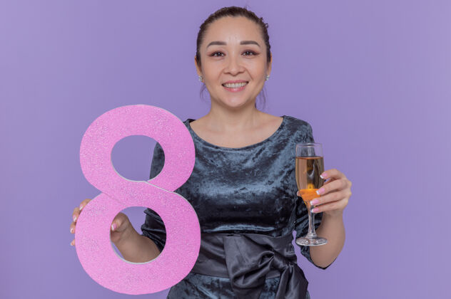 香槟快乐的亚洲女人拿着用硬纸板和香槟制成的8号 站在紫色的墙上 看着前面 微笑着欢庆国际妇女节亚洲制造欢呼