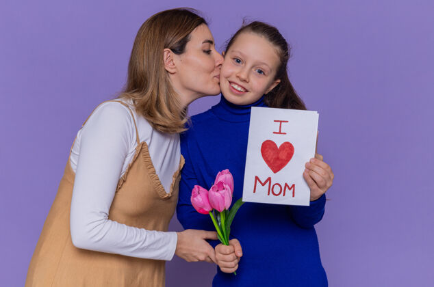 拥抱快乐的母亲微笑着亲吻她 快乐的斗士手持贺卡和郁金香花站在紫色的墙上庆祝国际妇女节亲吻国际女人