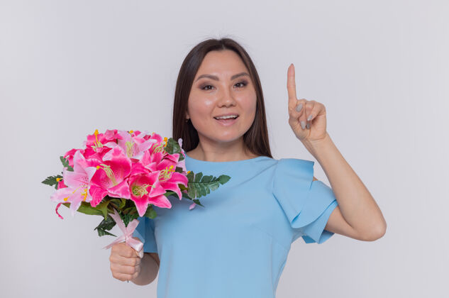 欢呼亚洲妇女手捧花束 满脸欢笑 伸出食指 站在白色的墙上庆祝国际妇女节亚洲庆祝站立