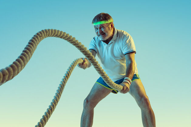 老年人高级男子在霓虹灯下用绳索在斜坡墙上训练身材魁梧的高加索男模保持活跃 运动运动的概念 活动 运动 健康 健康的生活方式篮球姿势活跃