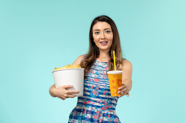 戏院正面图年轻的女性拿着篮子和薯片 在浅蓝色的表面上喝水餐具拿着水壶