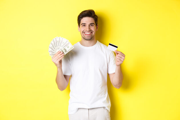 时尚年轻人从信用卡里取钱 微笑着高兴 站在黄色的背景上有钱金钱帅气