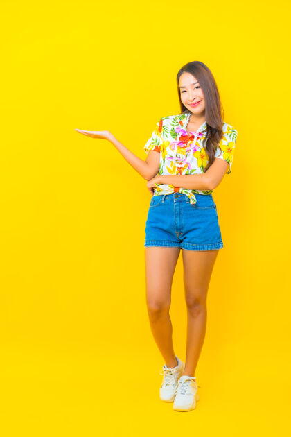 肖像美丽的亚洲年轻女子穿着彩色衬衫 在黄色的墙上展示什么的肖像微笑年轻旅游