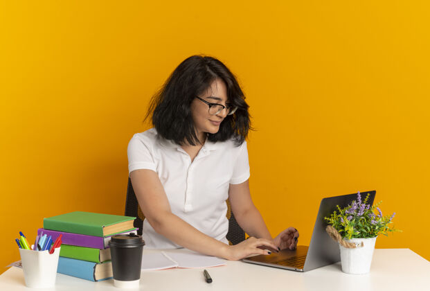 桌子年轻漂亮的白人女生戴着眼镜坐在书桌旁 手里拿着学习工具 看着笔记本电脑 笔记本电脑被隔离在橙色的空间里 还有复印空间看眼镜漂亮