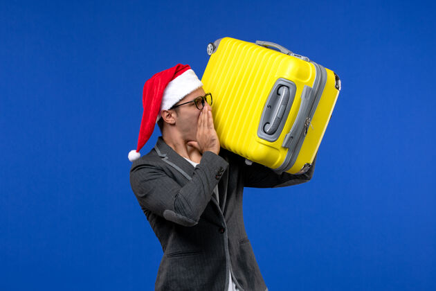 包正面图年轻男子提着沉重的黄色袋子在蓝色办公桌飞行飞机上度假工作工业圣诞节