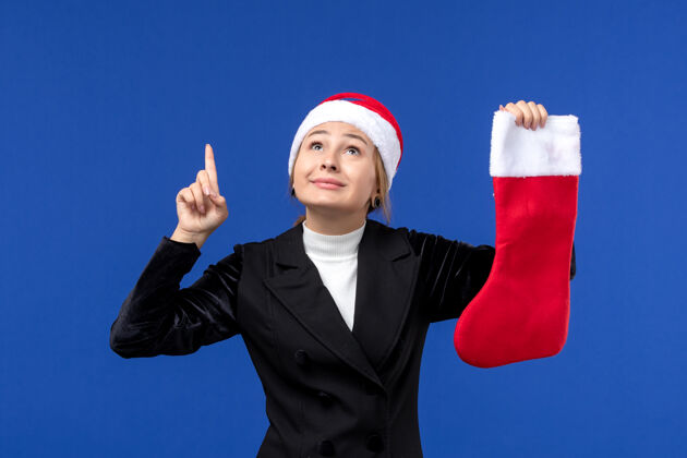 专业正面图年轻女子手持红色圣诞袜在蓝色墙壁上人类节日新年成功袜子年轻的女性