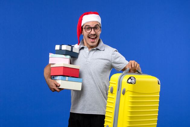 帽子正面图：年轻男性手持礼物和包在蓝色背景的飞机上度假人男性工人