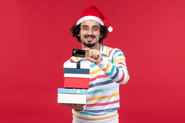 圣诞节正面图年轻男子拿着节日礼物和银行卡在红墙上压岁钱红可爱时尚女人