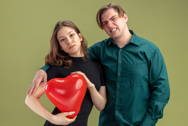 情人节一对年轻漂亮的情侣穿着休闲服 站在绿色的墙上 用心形气球庆祝情人节期待日子休闲