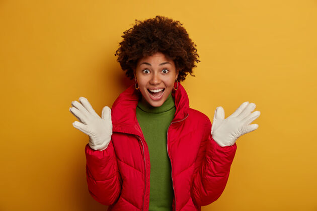 衣服快乐的少女摊开手掌 欢庆初雪 穿着红色外套和白色手套 在冬天欢笑 站在黄色的工作室墙上欢呼满意拍摄