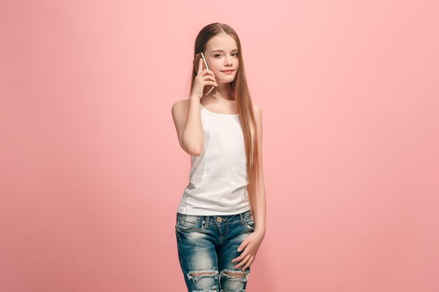 女士快乐的少女站着 微笑着用手机在时尚的粉红色工作室情感青少年女性