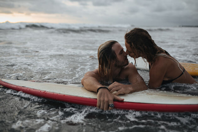 微笑日落时分在冲浪板上亲吻的迷人情侣冲浪板一起男性