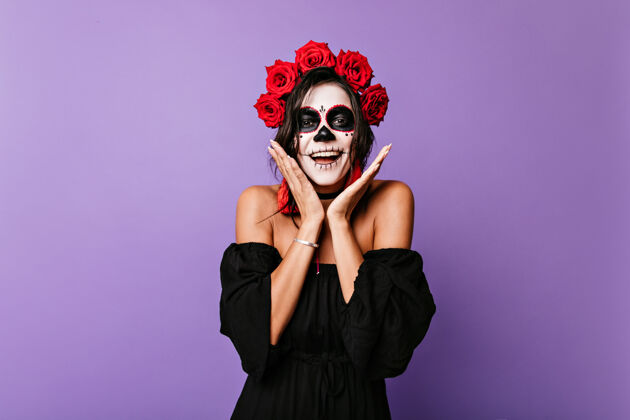 头骨一个穿着黑衣服 光着肩膀的晒黑女孩出其不意万圣节化妆的墨西哥模特的室内画像 头发上戴着鲜花花肖像女巫