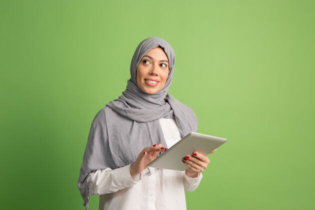 女士戴着头巾的快乐阿拉伯女人拿着笔记本电脑微笑女孩的肖像 在绿色工作室摆姿势肖像女性欢乐