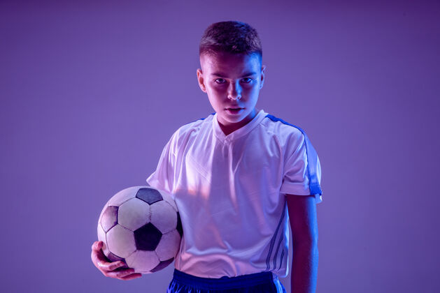 黑暗小男孩像个足球运动员一样站在黑暗的墙上设备跑步踢球