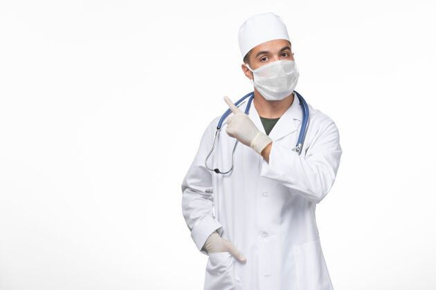 实验室外套正面图：男医生穿着医疗服 戴着防冠状病毒面罩 在浅白的墙壁上进行冠状病毒疾病隔离大流行大流行男性疾病