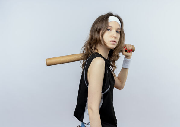 蝙蝠穿着黑色运动服的年轻健身女孩 头上戴着棒球棒 严肃的脸站在白色的墙上女孩站看