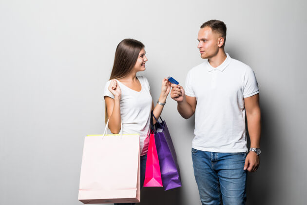 购物美丽的年轻微笑阳光学生夫妇举行了许多彩色购物袋隔离在白色背景丈夫一起包