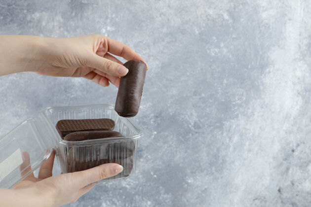 巧克力女人手里拿着一个塑料盒子 盒子里的巧克力奶油卷被隔离在大理石背景上堆栈卷华夫饼
