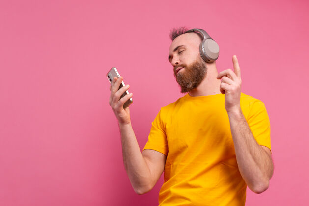 休闲帅哥带着手机和耳机在粉色背景上翩翩起舞微笑耳机情感