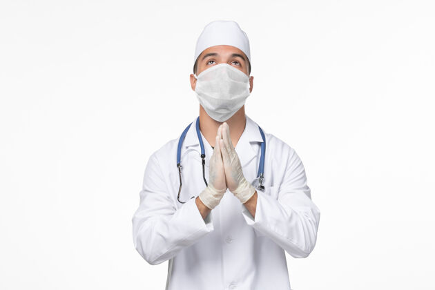 医疗正面图男医生身穿防毒服 戴着口罩祈祷白墙病毒冠状病毒-疾病大流行对抗疾病正面