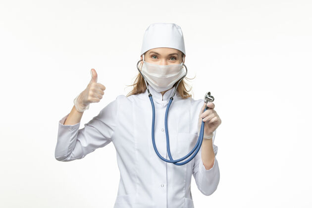 制服前视图穿着白色医疗服的女医生在白色办公桌上使用听诊器和微笑疾病共患大流行疾病微笑大流行使用