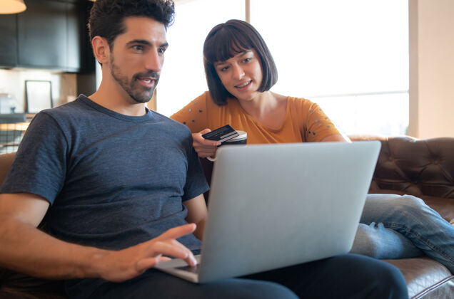 人一对年轻夫妇在家里用信用卡和笔记本电脑在线购物的照片电子商务概念新的正常生活方式笔记本电脑一起订购