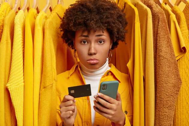 手机悲伤沮丧的非洲女人通过网上钱包付款 持有信用卡和现代手机包不高兴客户