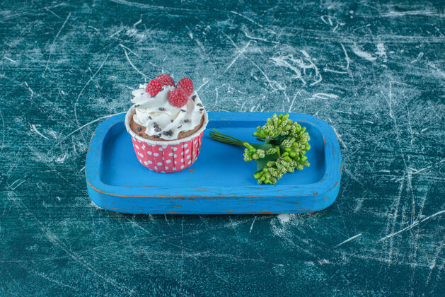 糕点一束花蕾和一个纸杯蛋糕放在蓝色背景的木盘上高质量的照片口感糖甜点