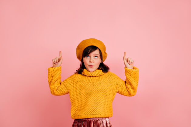 法国戴着黄色贝雷帽的无忧无虑的孩子抬起头来高加索孩子在粉红色的墙上做鬼脸时尚童年女孩