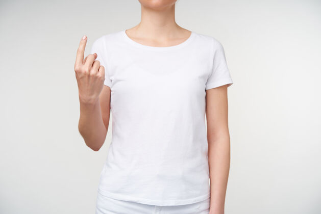 白色室内照片 年轻女士展示食指 同时在手语上表示单词的位置 隔离在白色背景上有听力障碍的人的手势符号站立休闲
