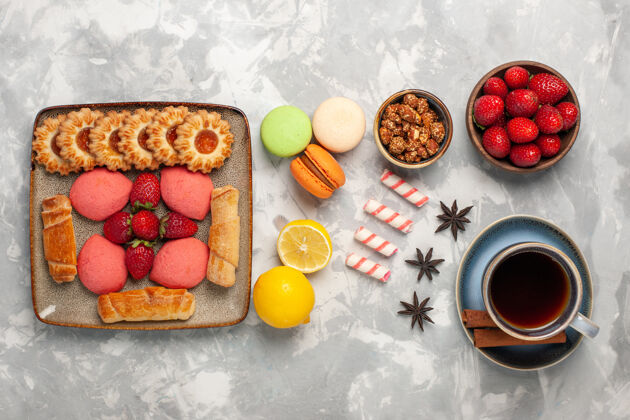 百吉饼白色桌面上有美味的百吉饼 蛋糕 茶 新鲜草莓 茶和饼干顶部糖早餐