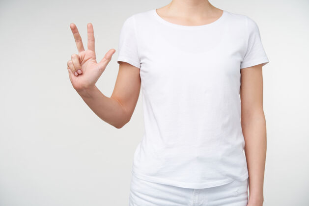 室内一张穿着休闲服的年轻女士站在白色背景上数着三个手指的室内照片人手和手势的概念年轻图形符号