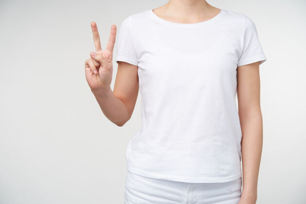 身体一个穿着休闲服的年轻女性在白色背景下摆姿势 举手形成胜利标志 用手指数着两个白色皮肤白皙女性