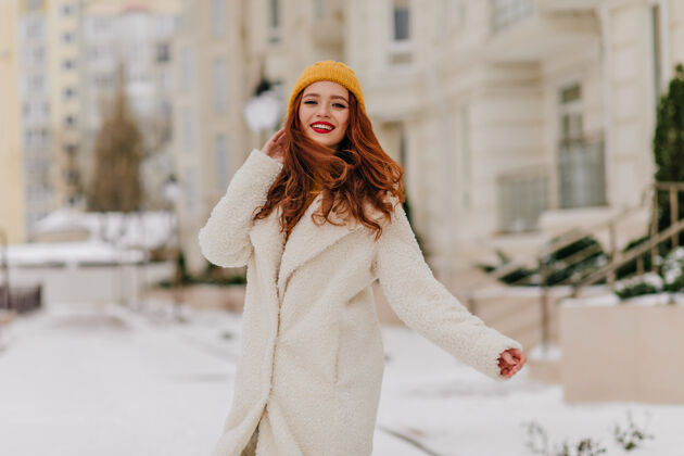 女孩令人惊艳的黄帽子长发女孩在模糊的街道上摆姿势快乐的姜女享受冬天的户外镜头兴奋姜帽子