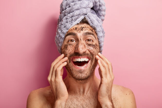美容男性美容概念快乐快乐的男人把咖啡擦在脸上 去除深色的宠爱 想看起来精神焕发 头上包了毛巾欧洲健康面膜