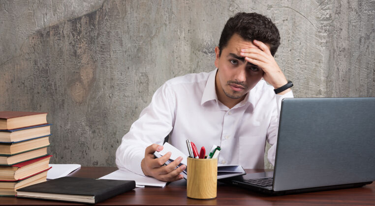办公室疲惫的员工坐在办公桌前 看着一张张纸高质量的照片员工笔记本电脑人