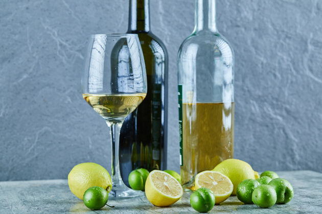 玻璃杯两瓶和一杯葡萄酒放在大理石桌上 上面放着柠檬和樱桃李子奢侈品李子大理石