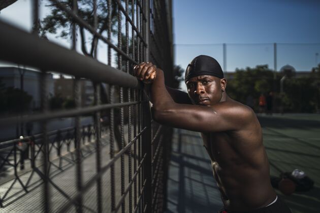 健美一个非洲裔美国男性半裸倚在篱笆上的浅焦镜头健康围栏户外