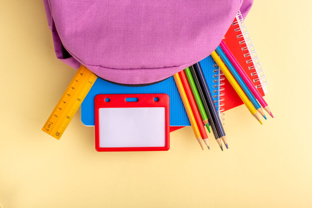 视图顶视图彩色铅笔与抄写本和紫色书包浅黄色书桌上的学校感觉笔铅笔本记事本教育光钢笔