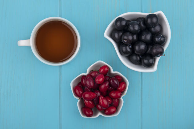 茶顶视图的水果 如山茱萸和树莓在碗与茶杯蓝色背景膳食食物顶部