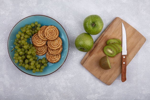 苹果顶视图用刀在砧板上切猕猴桃片 绿色苹果 绿色葡萄和饼干放在白色背景的盘子上猕猴桃板视野