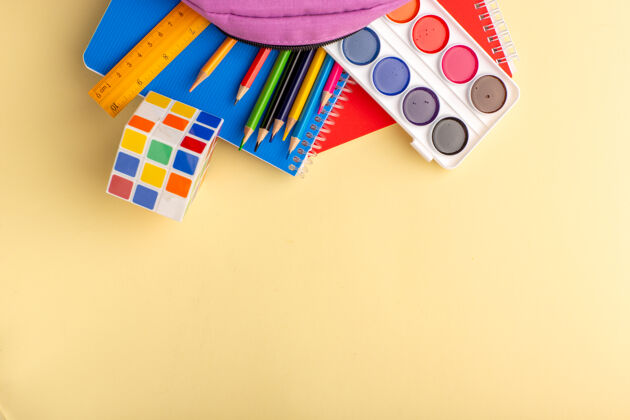 五颜六色顶视图彩色铅笔与抄写本油漆和浅黄色书桌上的紫色包学校毛毡笔铅笔本记事本包钢笔桌子